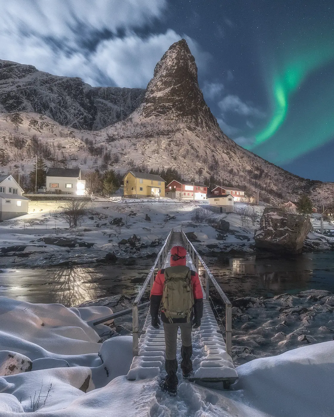 Landscape photographer walking in snowy Lofoten village beneath northern lights during winter photography experience