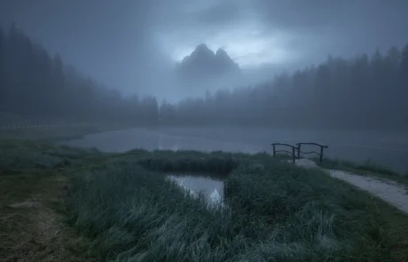 Misty sunrise landscape in the Dolomites with lake, fog and mountain peaks emerging through clouds