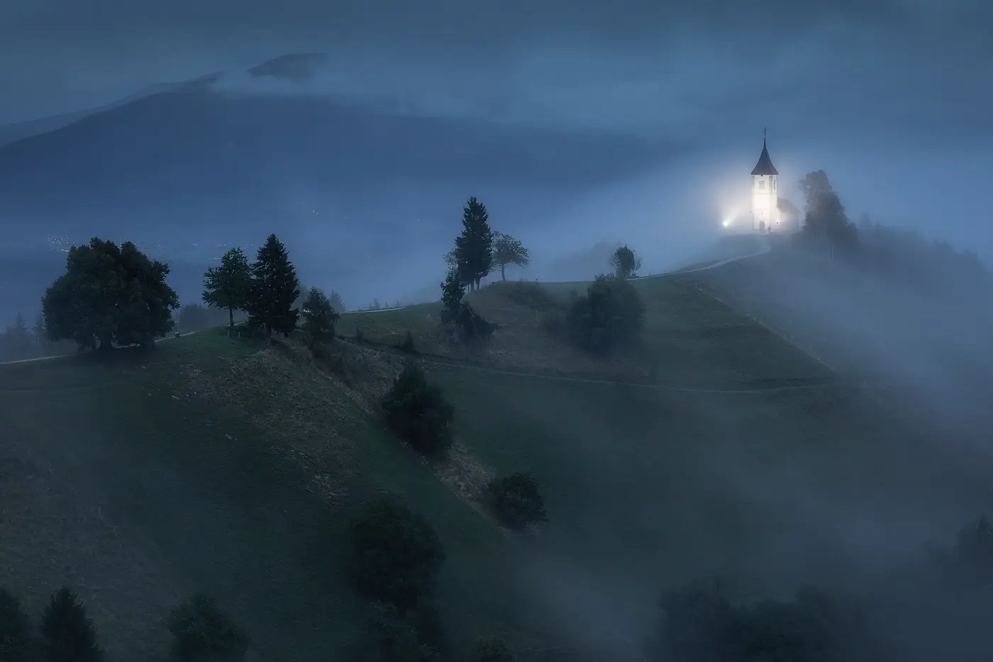 Private Slovenia Photography Tour – Misty Morning Landscape Misty blue hour scene in Slovenia with a church emerging from the fog