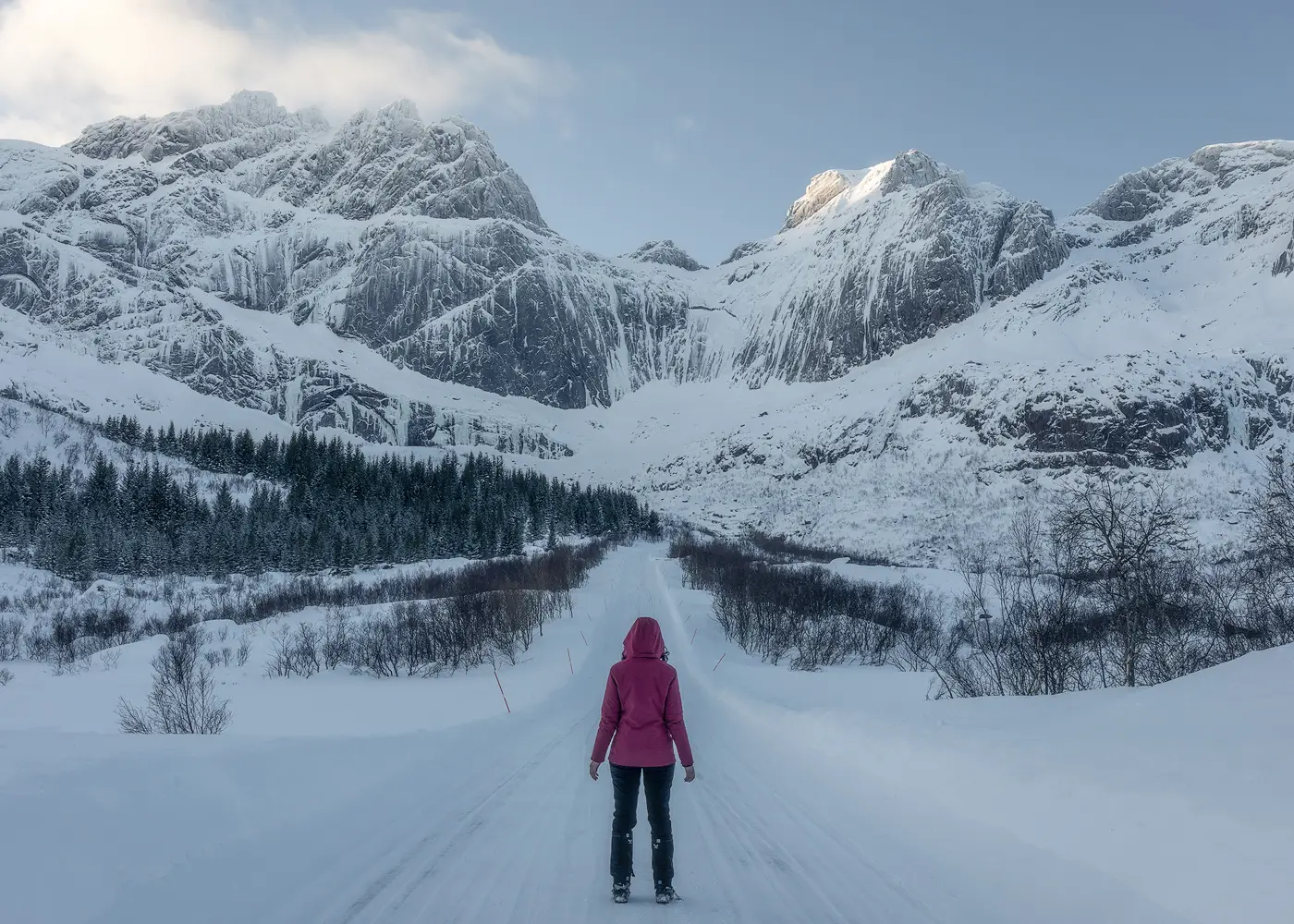 Winter Road Exploration, Norway Traveller standing on a snowy road surrounded by dramatic winter mountains in Norway. Atmospheric landscape photography for editorial and tourism use.
