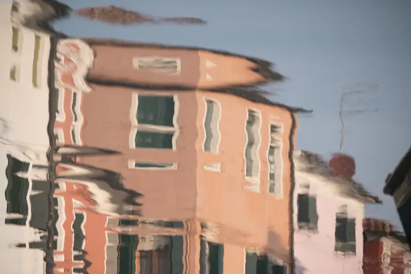 Abstract reflection of pastel-coloured houses in Burano, Venice, distorted by gentle ripples in the lagoon water.