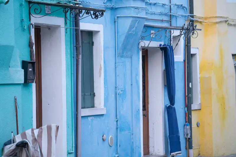 Colourful blue and yellow houses along a quiet residential street in Burano, Venice, with traditional details and pastel facades.