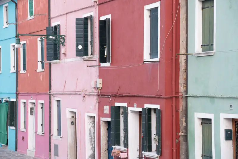 Colourful pastel houses lining a quiet street in Burano, Venice, with traditional facades and vibrant architecture.