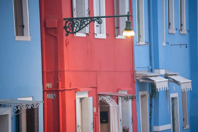 Colorful houses and a traditional street lamp glowing at blue hour in Burano, Venice.