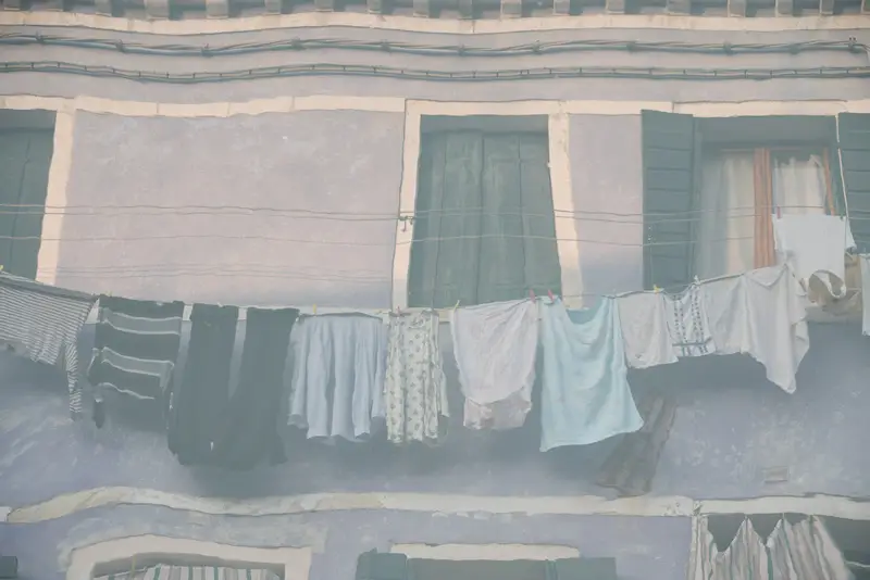 Reflections of hanging laundry and pastel-coloured houses distorted by the waters of a canal in Burano, Venice.