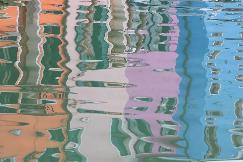Abstract reflection of colourful Burano houses in the water, creating pastel patterns and flowing shapes in the Venetian Lagoon.