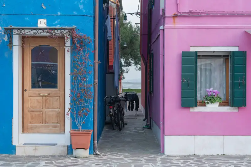 Colourful houses and a narrow alley leading towards the Venetian Lagoon in Burano, Venice.