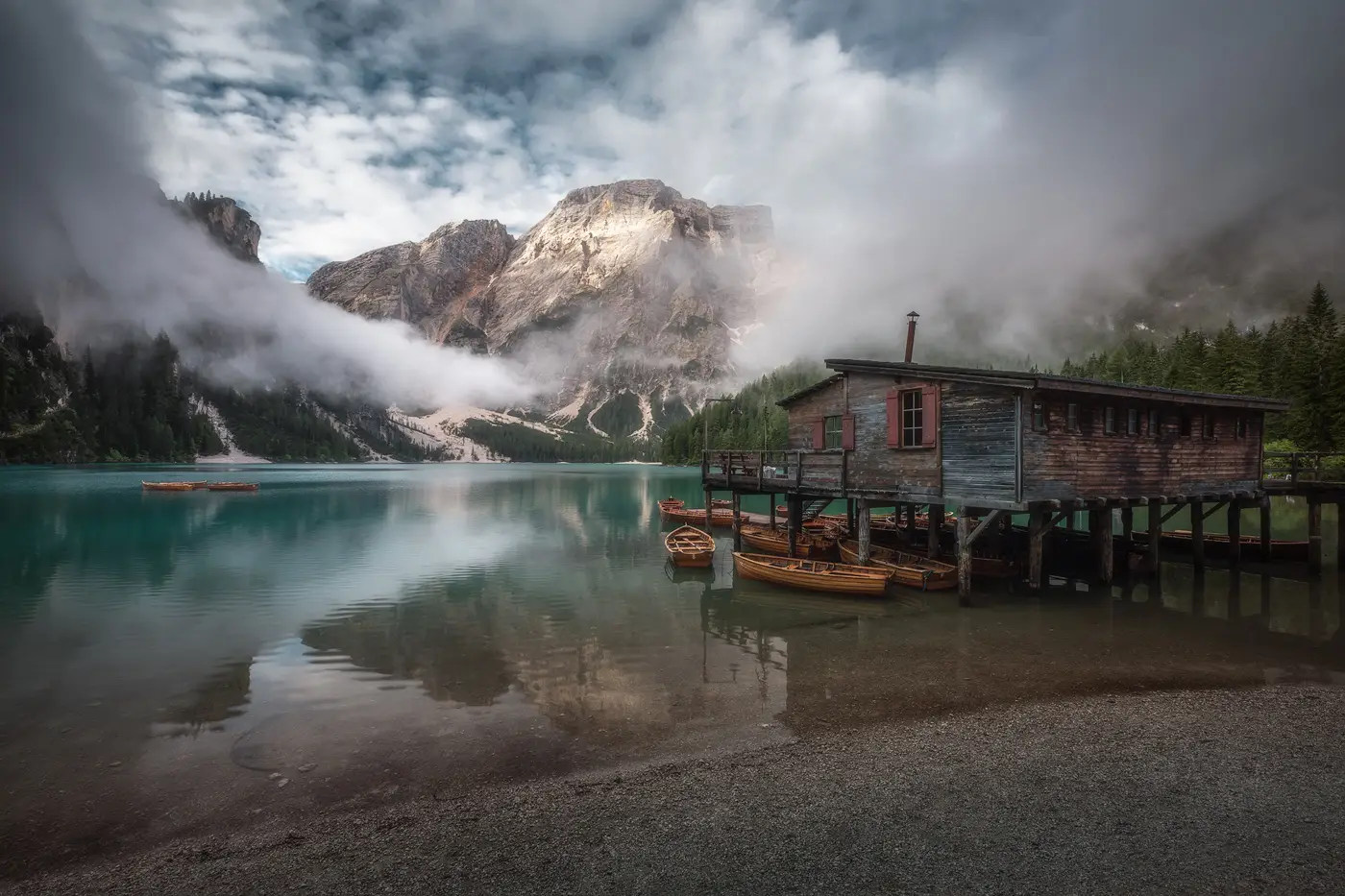 Boathouse and wooden boats at Lago di Braies surrounded by misty mountains in the Dolomites, Italy
