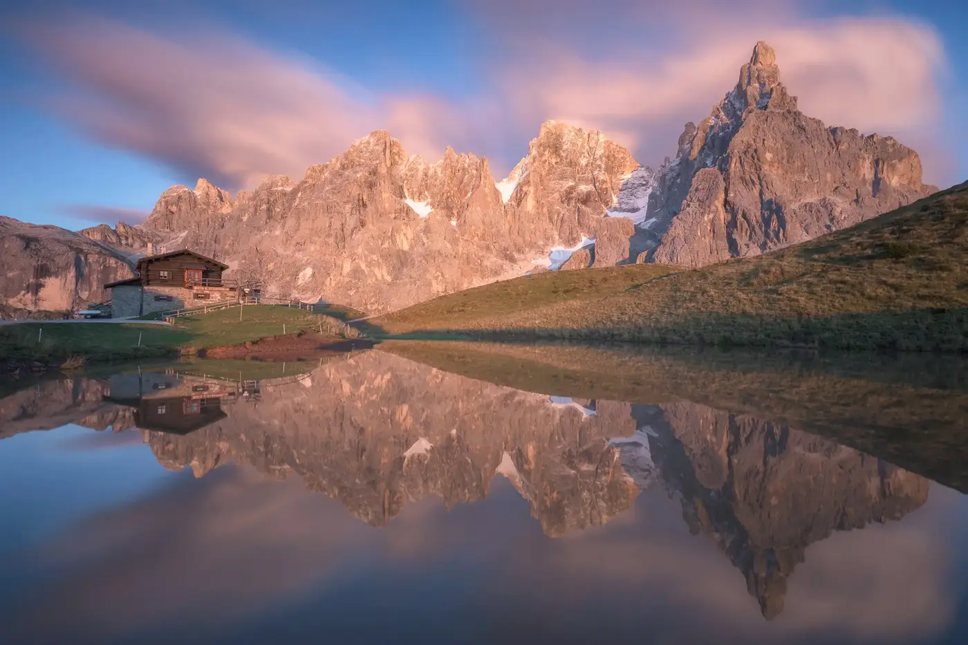 Baita Segantini reflected in an alpine pond with the Pale di San Martino peaks at sunrise near Passo Rolle in the Dolomites, Italy