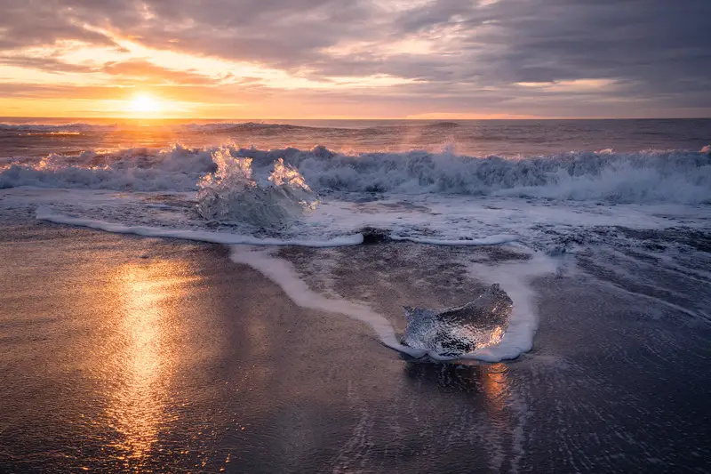 Ice block on Diamond Beach with breaking waves at sunrise, Iceland.