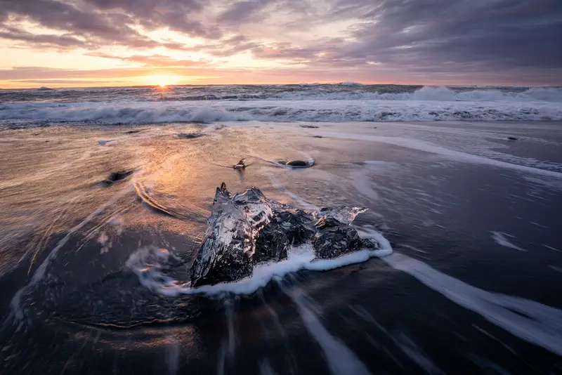 Ice block surrounded by flowing waves at sunrise on Diamond Beach, Iceland.