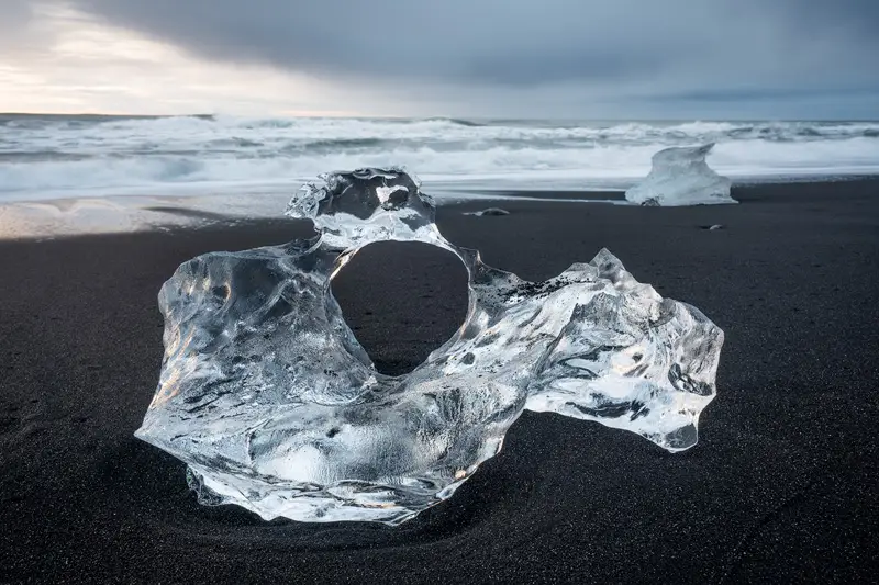 Crystal-clear ice block with a natural circular hole on Diamond Beach, Iceland.