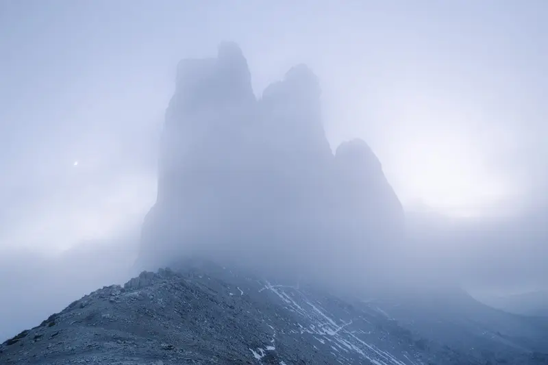 Tre Cime di Lavaredo emerging through fog at twilight in the Italian Dolomites