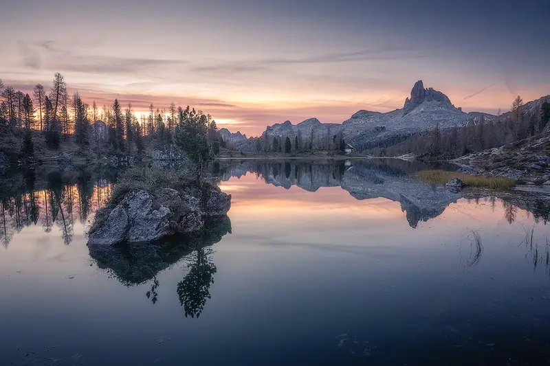 Croda da Lago reflected in Lago Federa at sunrise, with autumn larch trees and pastel skies in the Dolomites