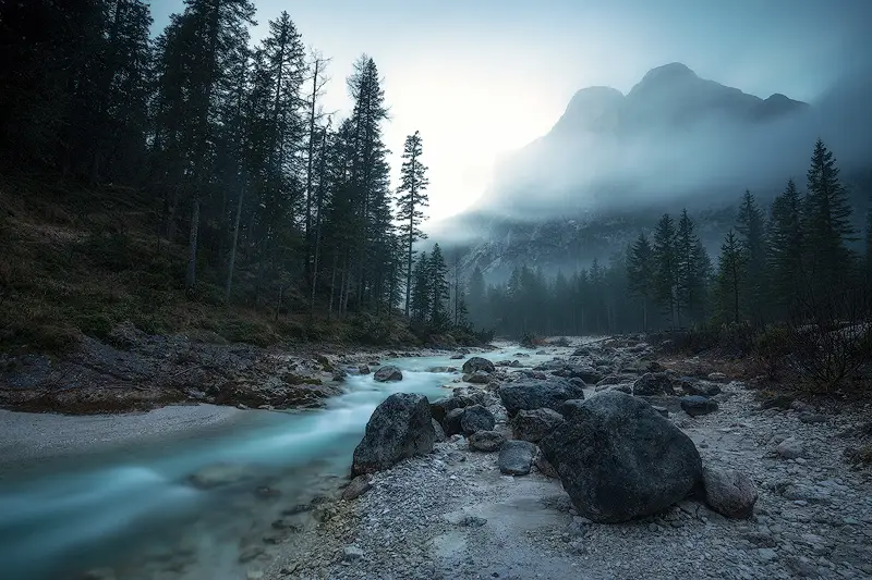 Mountain stream flowing through a rocky forest valley near Fanes Waterfalls, with mist surrounding the Dolomites peaks near Cortina d'Ampezzo.