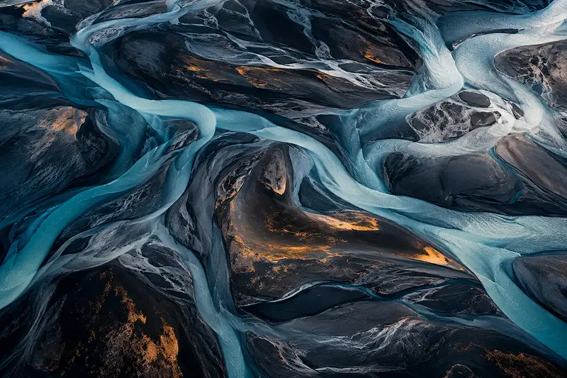 Abstract aerial view of turquoise glacial rivers winding through dark volcanic sands, creating intricate natural patterns inspired by Iceland