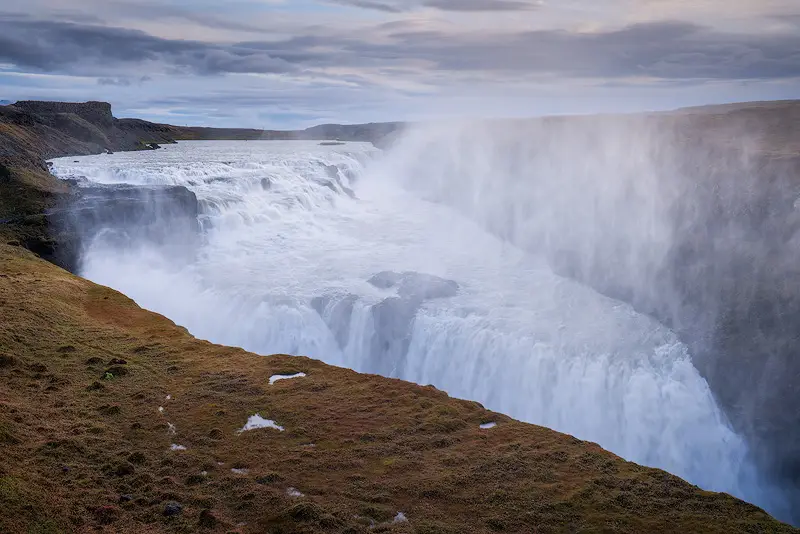 Gullfoss waterfall in Iceland with powerful glacial waters cascading into a deep canyon beneath cloudy skies