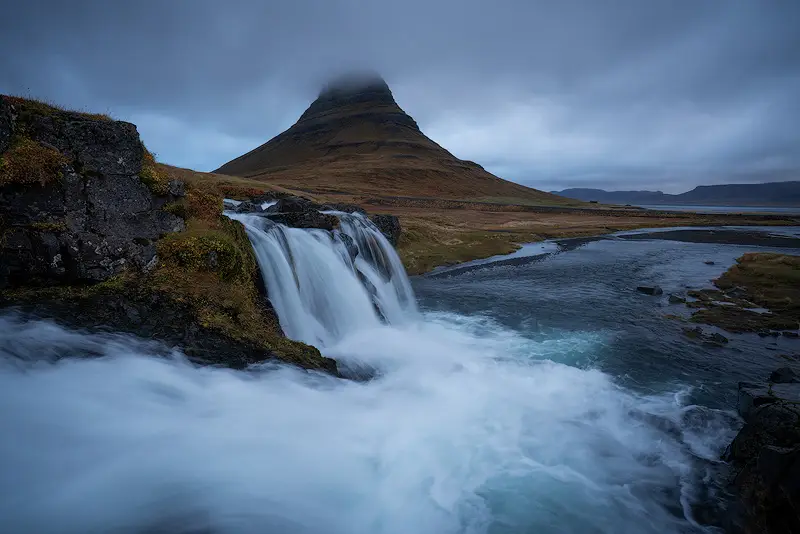 Kirkjufell mountain and Kirkjufellsfoss waterfall beneath dramatic cloudy skies in Snæfellsnes, Iceland