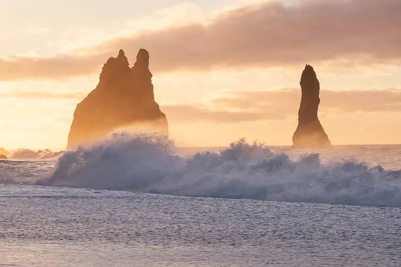 Reynisdrangar sea stacks rising above Atlantic waves in golden light at Reynisfjara Beach, Iceland