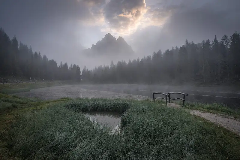 Misty sunrise at Lago d'Antorno in the Italian Dolomites, with mountain peaks emerging through low clouds