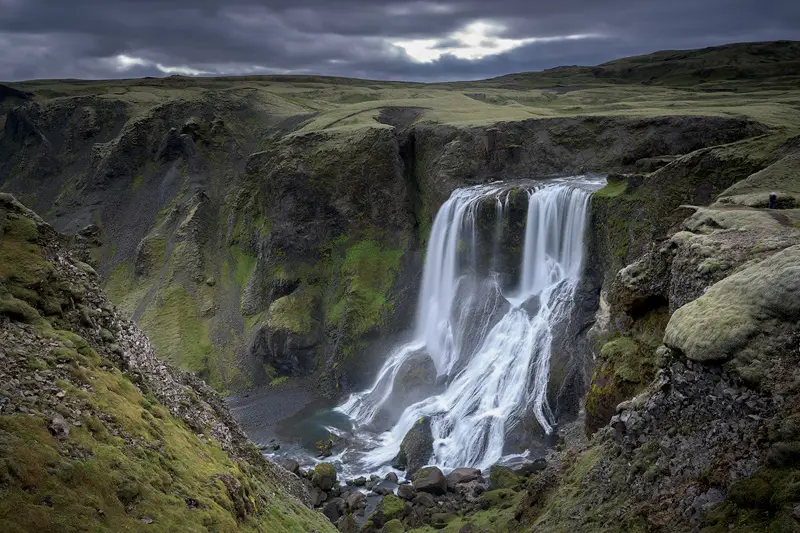 Fagrifoss waterfall plunging into a moss-covered volcanic gorge beneath storm clouds in the Icelandic Highlands.