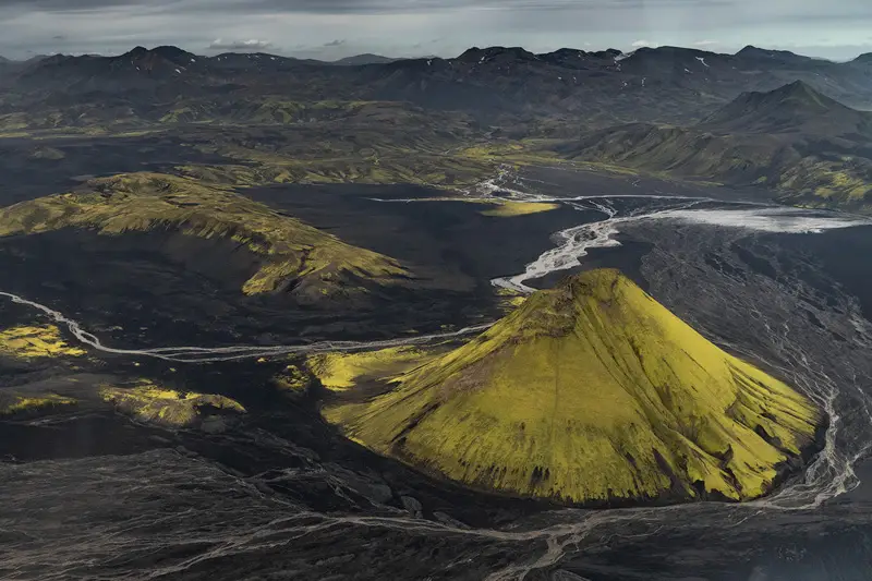 Aerial view of a moss-covered volcanic cone surrounded by black lava fields and winding rivers in Lakagígar, Icelandic Highlands.