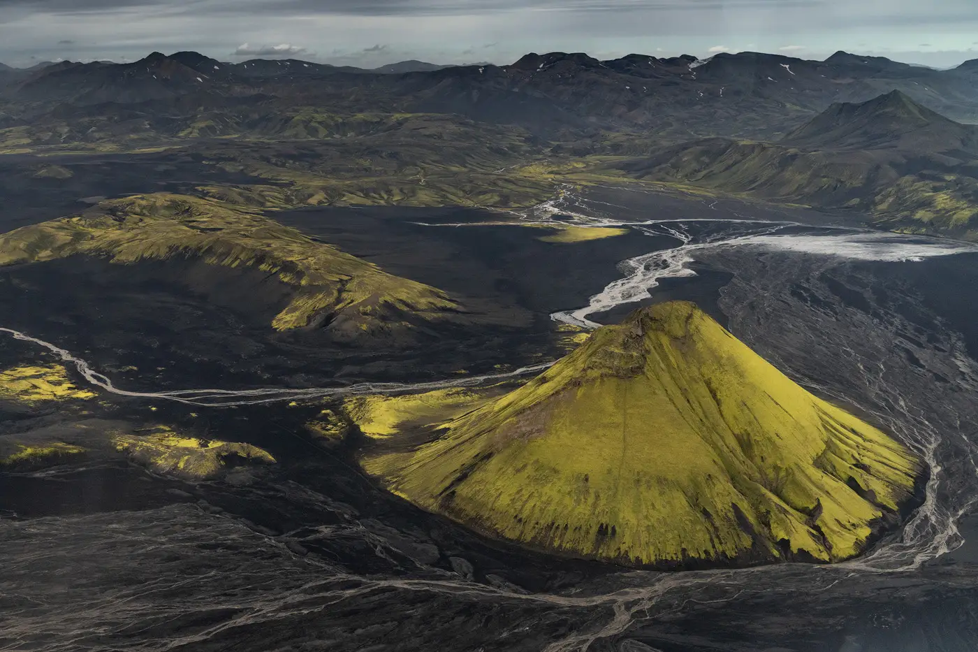 Aerial view of a moss-covered volcanic cone surrounded by black lava fields and winding rivers in Lakagígar, Icelandic Highlands.