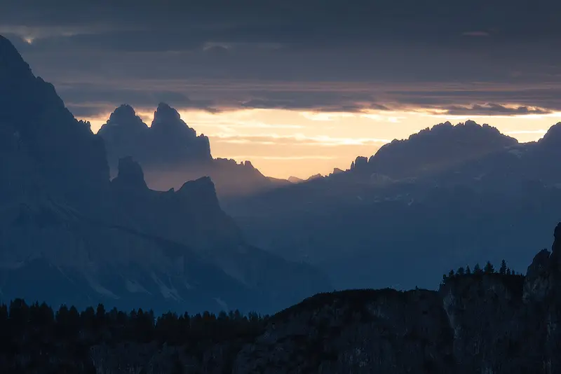 Layered Dolomites mountain peaks silhouetted against golden sunrise light near Passo Giau, Italy.
